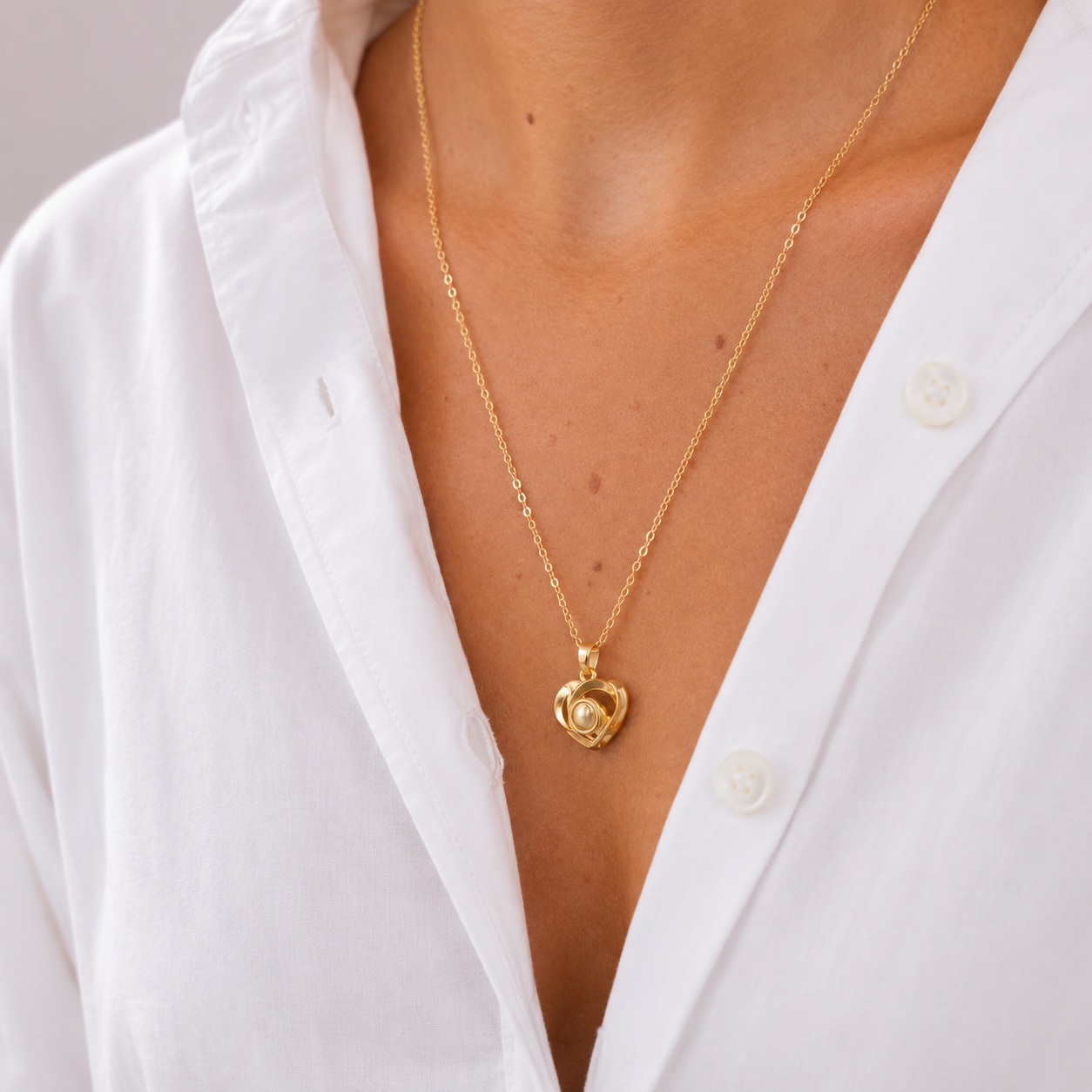 Gold heart pendant with pearl, worn on a white shirt